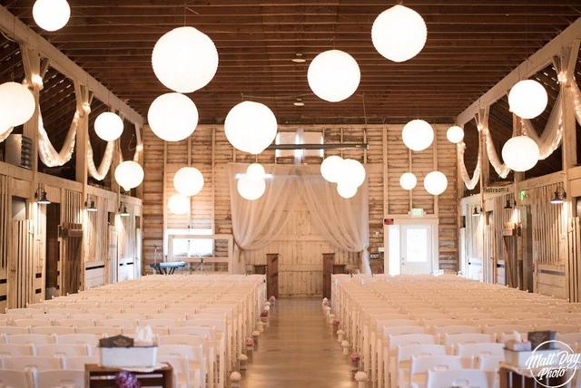 Barn set for an indoor ceremony with white chairs and lanterns