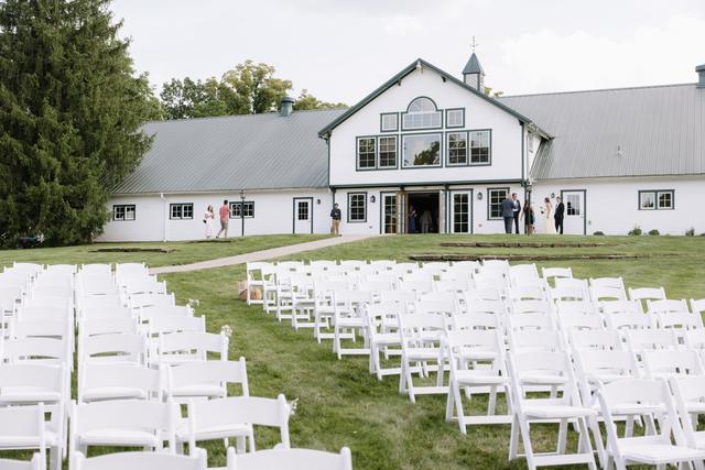 White ceremony chairs set on the lawn facing the white barn