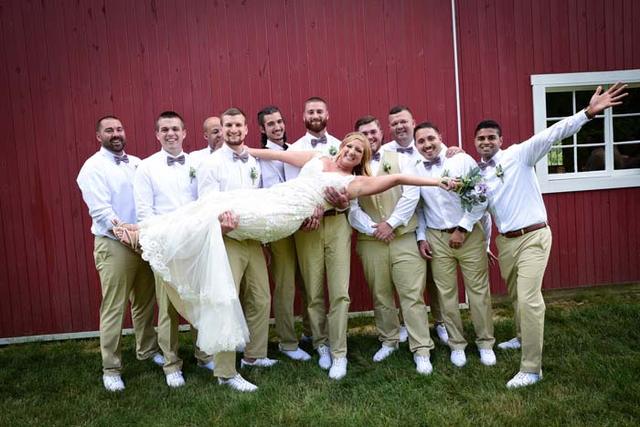 Groomsmen holding the bride in front of the red barn