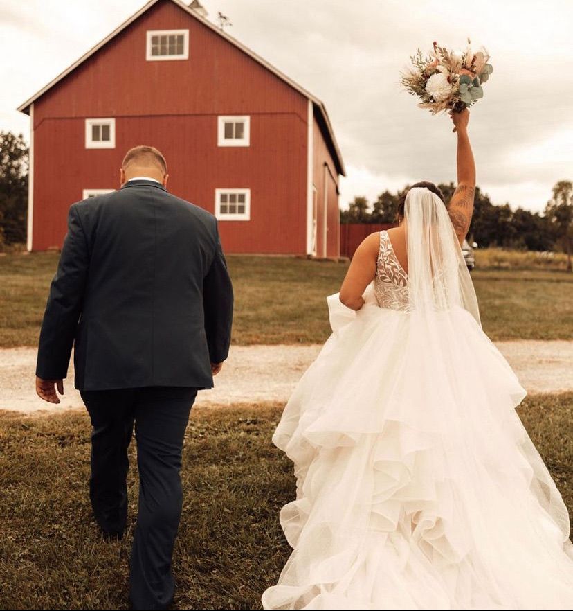 Bride raises her bouquet as the couple walks toward the little red barn