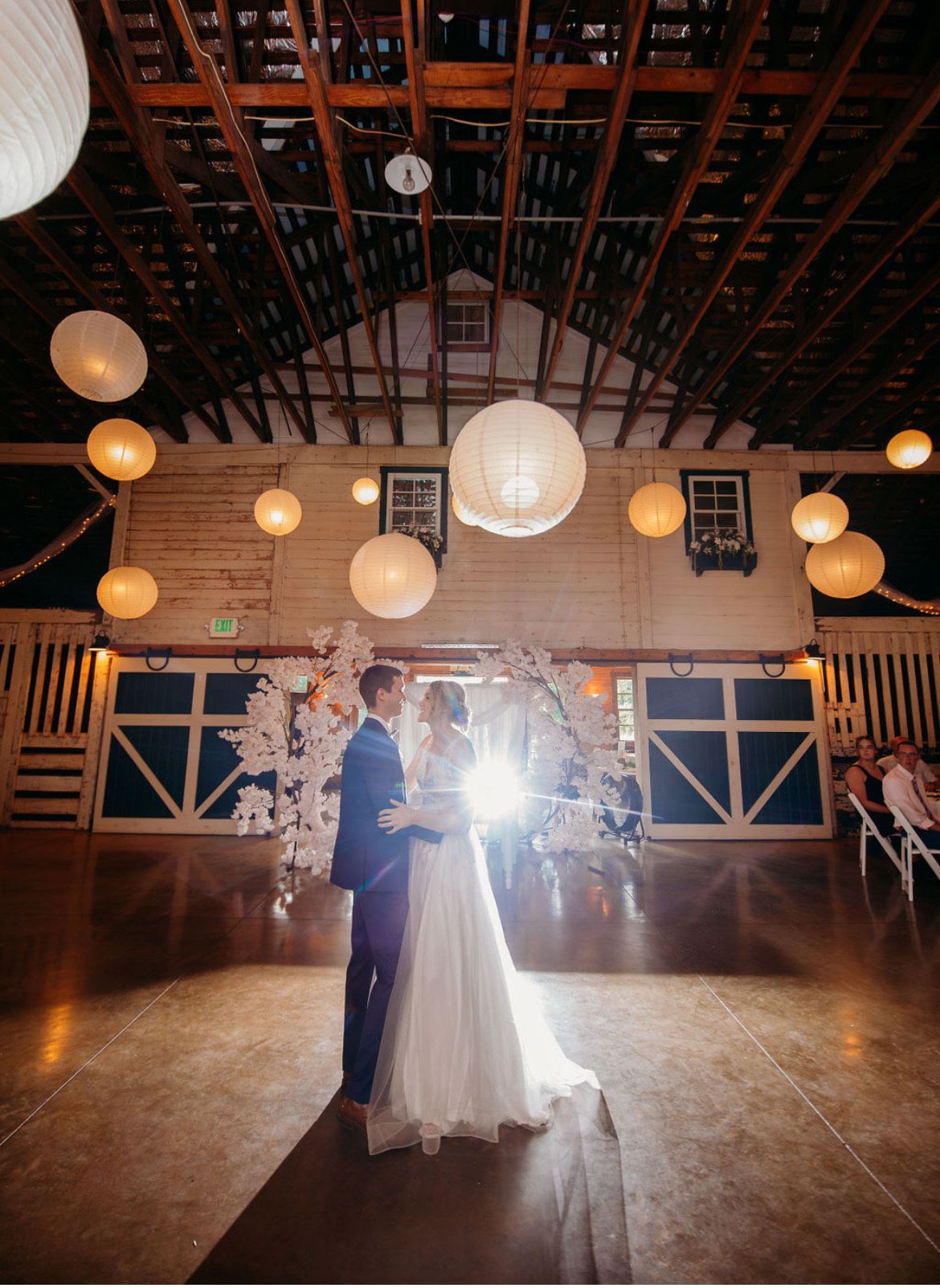 First dance beneath a lantern lit barn ceiling with a sunburst of light