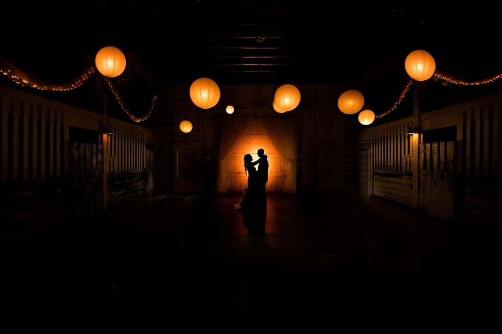 Couple silhouetted in a first dance at the end of the barn under glowing paper lanterns