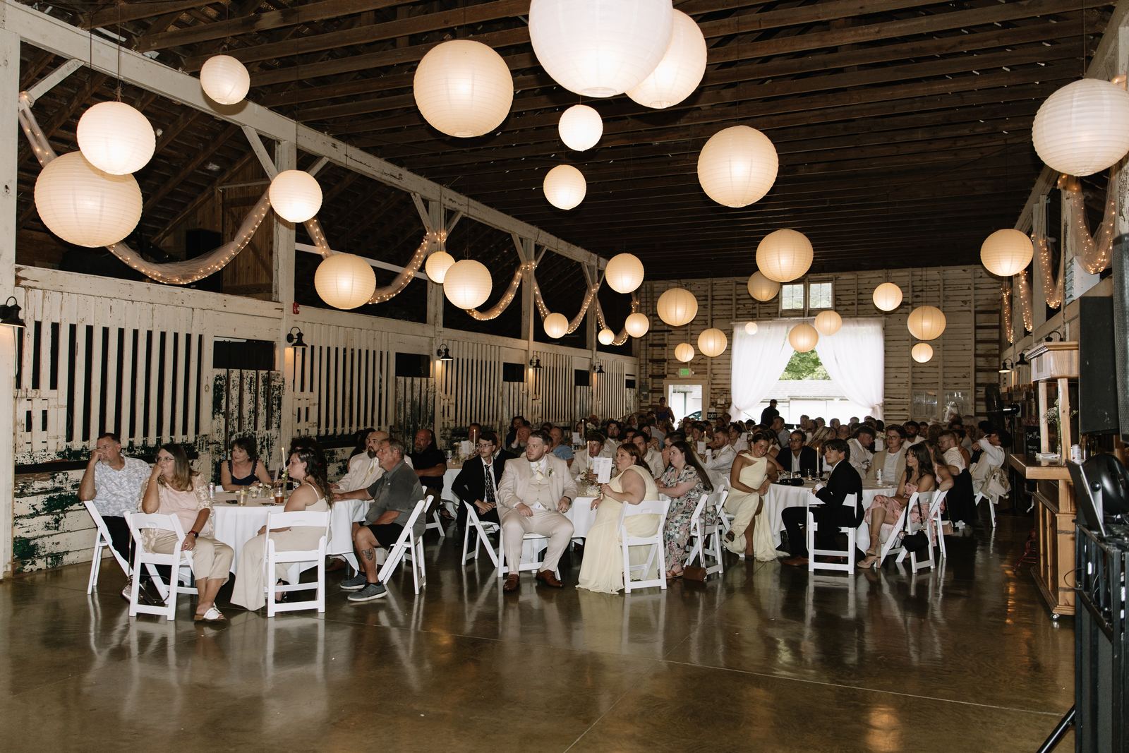 Guests seated at round tables in the barn beneath glowing paper lanterns