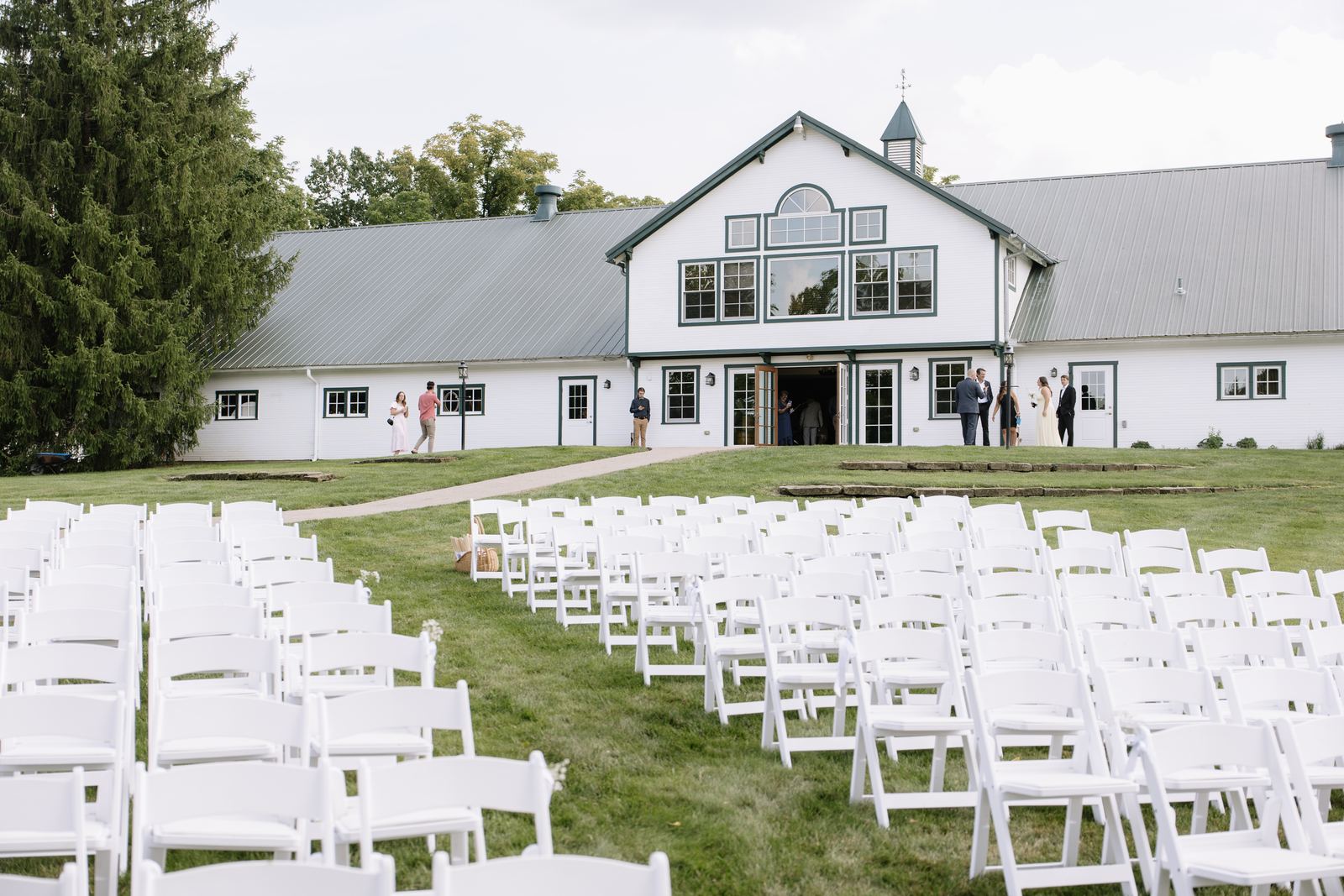 White ceremony chairs set on the lawn facing the white barn