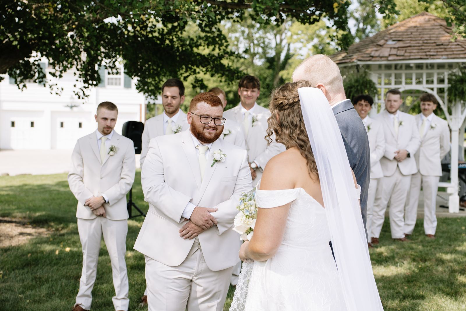 Groom smiling as the bride arrives at the ceremony with the gazebo behind