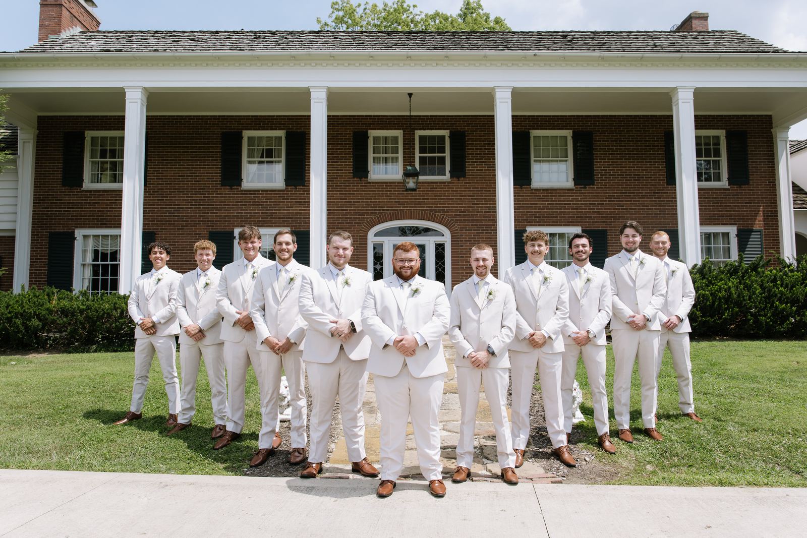Groom and groomsmen in front of the columned brick house