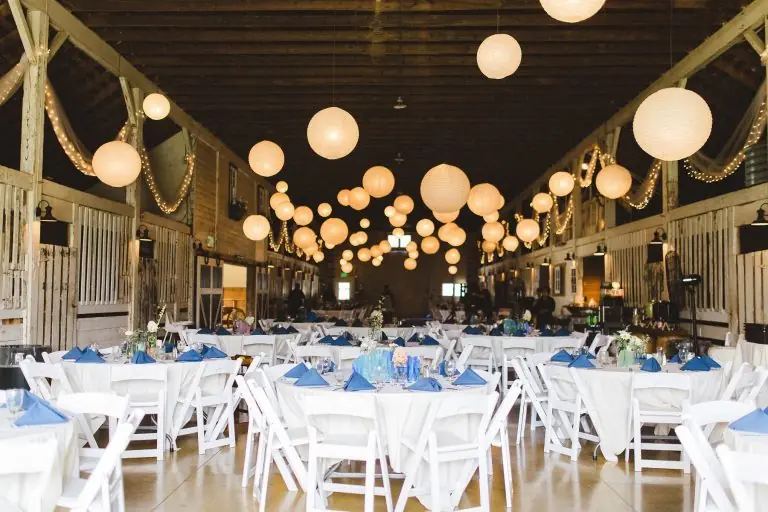 Barn reception tables set with blue linens under lanterns