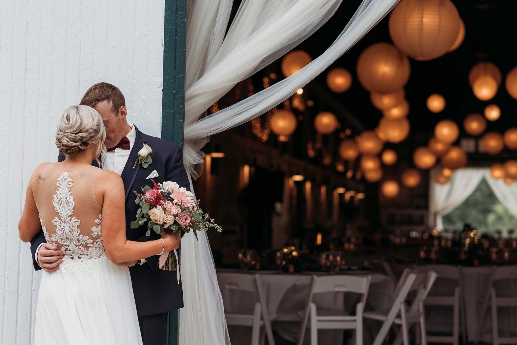 Bride and groom embracing at the barn doors with glowing paper lanterns inside