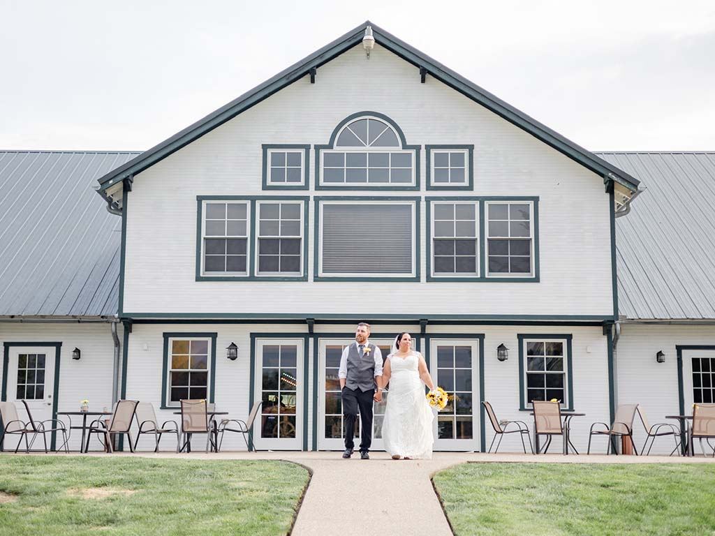 Bride and groom walking hand in hand from the front of the white barn