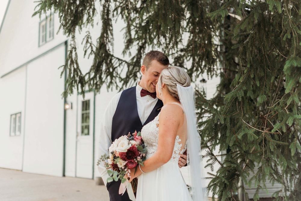 Bride and groom under the spruce tree beside the white barn